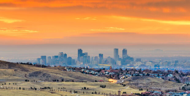 Denver city skyline is seen from afar with hills in the foreground at sunset