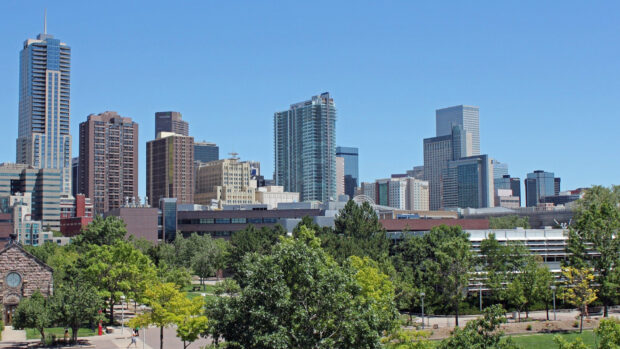 A clear view of Denver skyline with tall buildings and lush green trees in the foreground