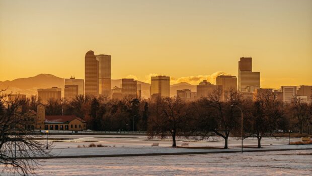 Denver skyline with snowy park and mountain backdrop at sunset