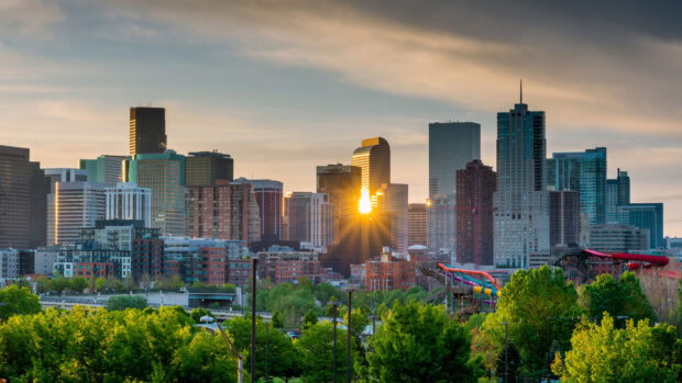 Denver skyline with sun reflecting on buildings and green trees in the foreground