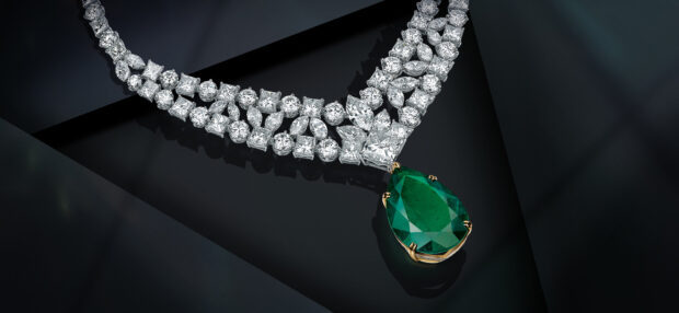 A luxurious diamond necklace with a large green gemstone pendant displayed on a black surface