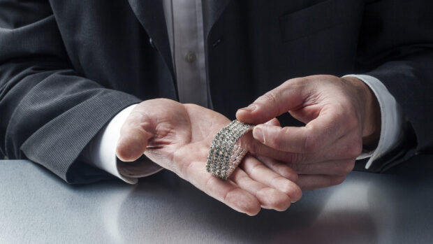 A man holding a diamond jewelry bracelet in his hand with a suit jacket sleeve visible