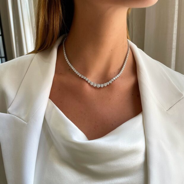 A close up of diamond jewelry necklace on a woman wearing white clothing