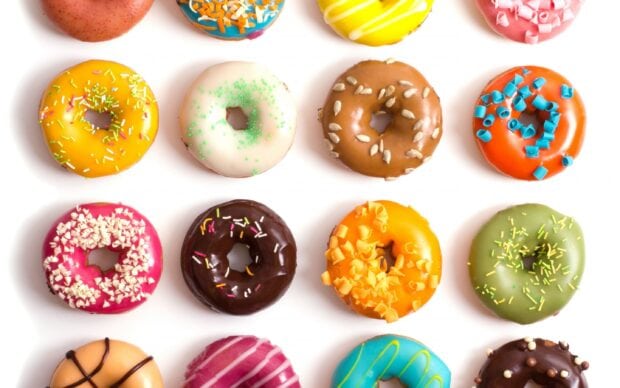 A collection of colorful donuts with various toppings arranged in rows on a white surface