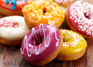 A close up of colorful donut with purple yellow and white frosting on a wooden surface