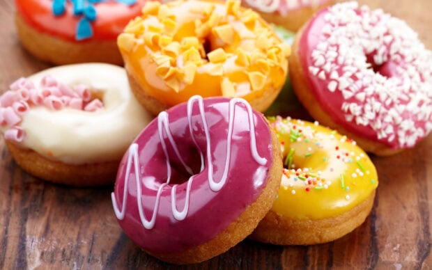 A close up of colorful donut with purple yellow and white frosting on a wooden surface