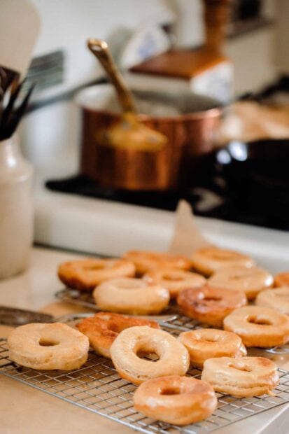 Fresh glazed donuts cooling on a wire rack in a kitchen setting