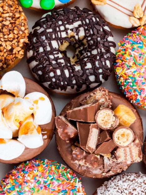 A close up of a chocolate donut topped with assorted candies and a chocolate donut with white icing