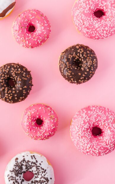 Pink and chocolate donuts with sprinkles on a pink surface