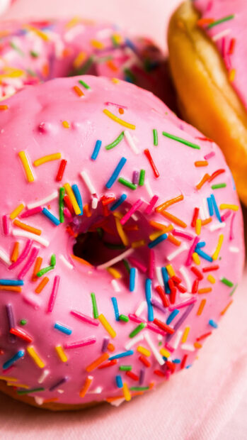 Close up of colorful sprinkled donut with pink glaze on a soft surface