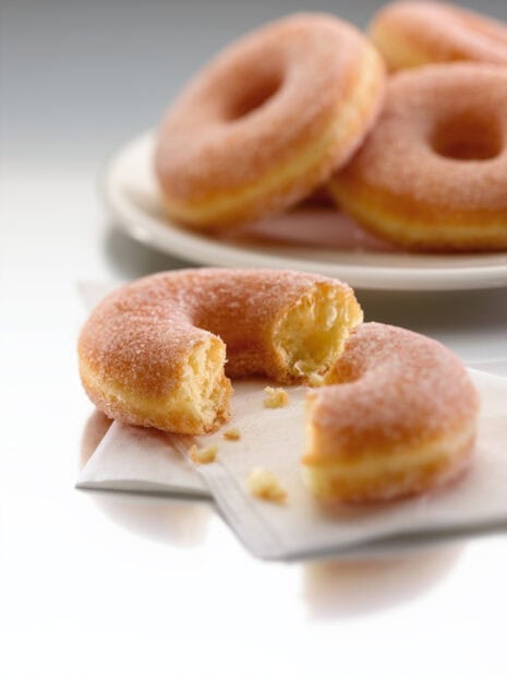 A bitten sugar donut with crumbs on a napkin and more donuts on a plate in the background