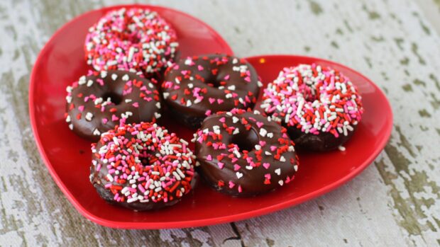 Chocolate donuts with colorful sprinkles on a red heart shaped plate