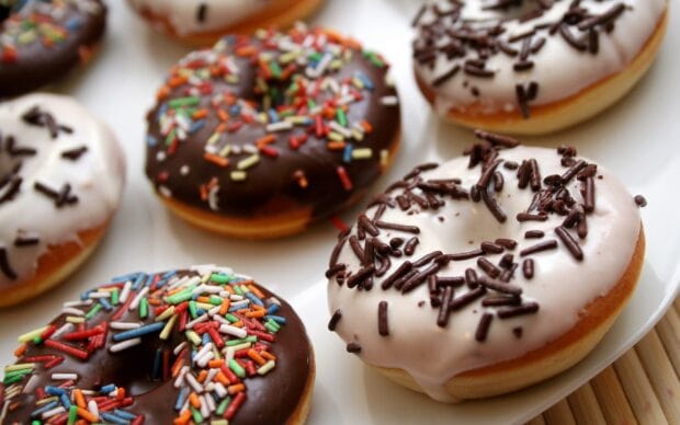 A close up view of donut with chocolate and colorful sprinkles on a white plate