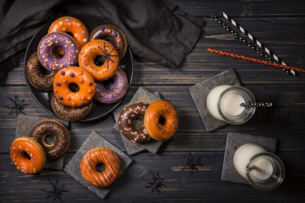 A variety of colorful donut decorated with Halloween sprinkles on a dark wooden table