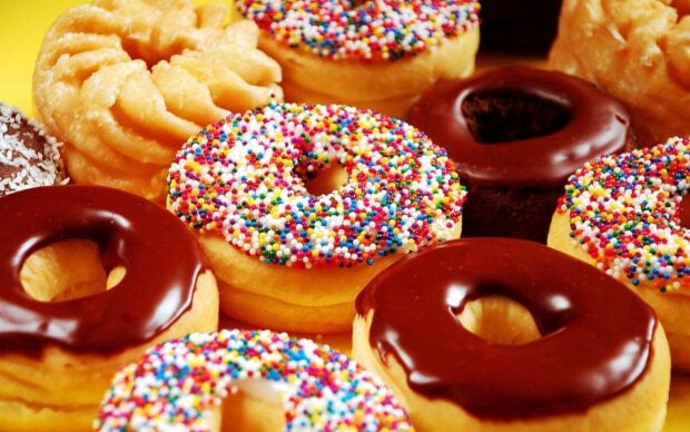 Close up of colorful donut with sprinkles and chocolate glaze on a bright yellow surface