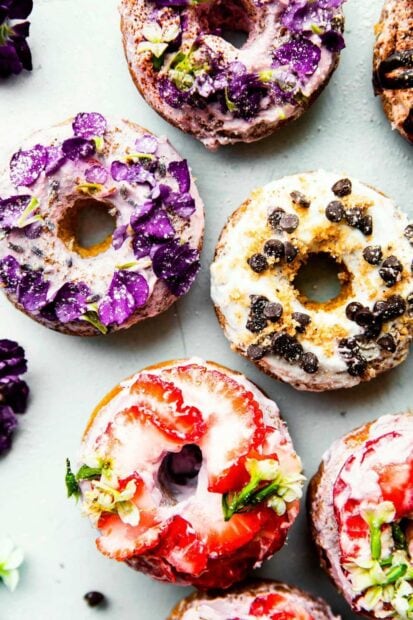 A close up of donuts topped with strawberry slices and purple flowers as edible decoration