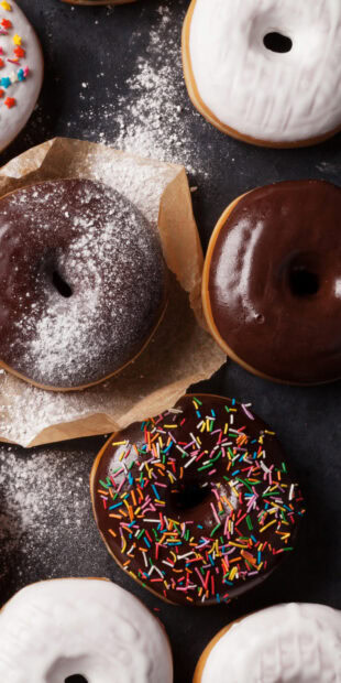 Chocolate donut with colorful sprinkles among assorted frosted donuts on a dark surface