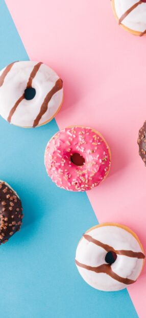 Colorful donut with sprinkles and icing on a pink and blue surface