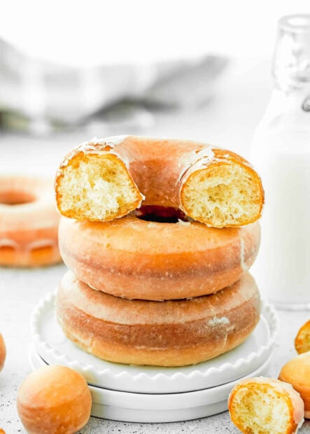 Soft glazed donut stacked with a bitten donut on top and donut holes on a white plate