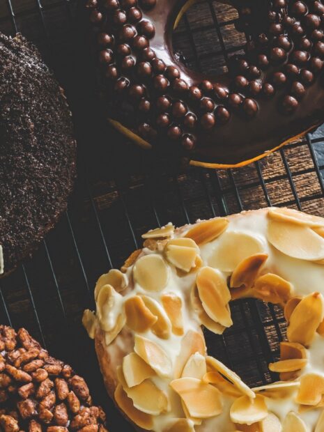 A close up of a donut with almond slices and creamy topping on a cooling rack