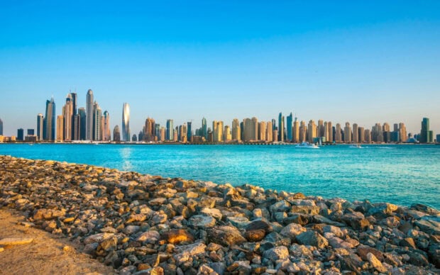 The Dubai skyline viewed from rocky shore with blue sea under clear sky