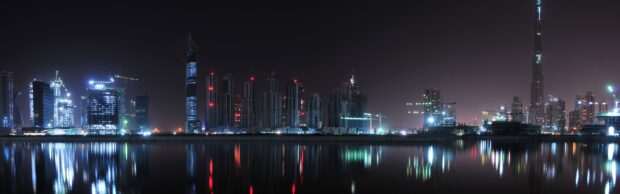 Night view of Dubai skyline with illuminated skyscrapers reflecting on water