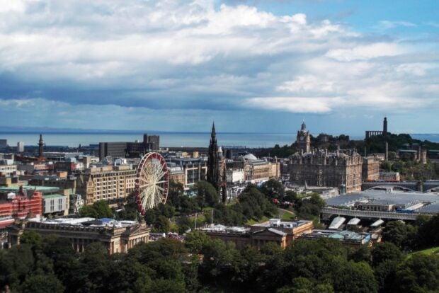 A stunning view of Edinburgh skyline featuring historic buildings and a Ferris wheel under cloudy skies