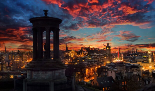 Edinburgh skyline at sunset with historic Dugald Stewart monument in the foreground and vibrant city lights