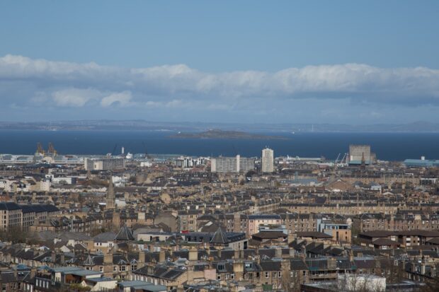 A detailed view of Edinburgh skyline showing historic buildings and distant sea under a blue sky