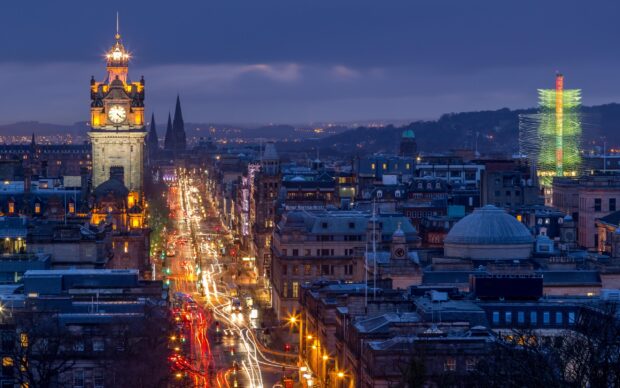 The Edinburgh skyline at dusk featuring the iconic clock tower and city lights along the main street
