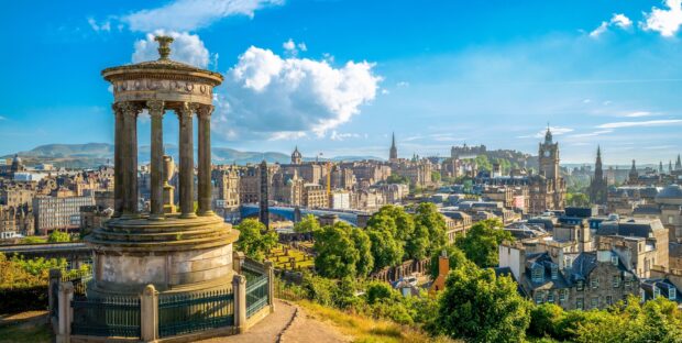 View of Edinburgh skyline with historic monument and cityscape under a bright blue sky