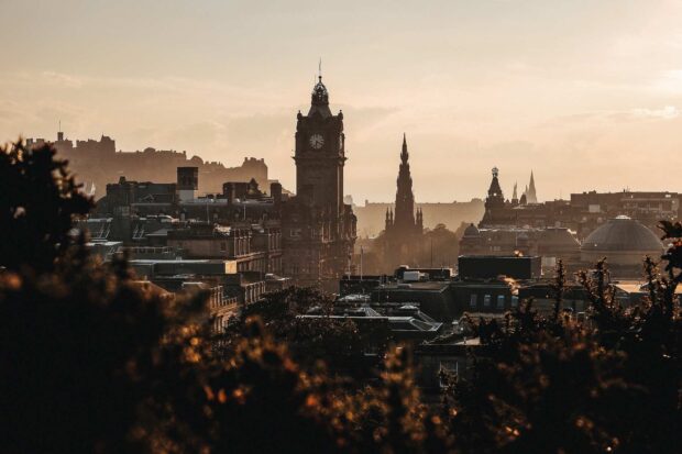 The historic Edinburgh skyline features iconic buildings in a warm sunset glow