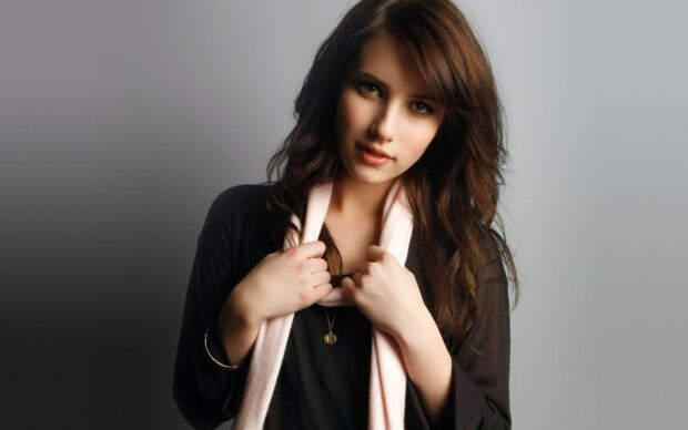 Emma Roberts wearing a black top and light scarf posing against a gray background