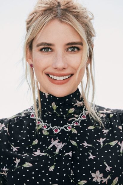 Emma Roberts wearing a black floral dress with a heart necklace smiling brightly
