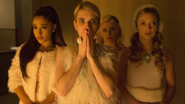 Emma Roberts standing with three women in a dimly lit room showing a shocked expression