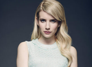 Emma Roberts wearing a light blue sleeveless top posing confidently against a dark background