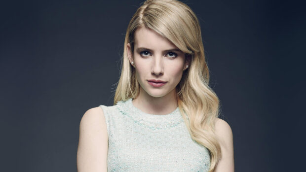 Emma Roberts wearing a light blue sleeveless top posing confidently against a dark background