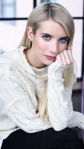 Close up of Emma Roberts wearing a white knitted sweater and looking at the camera
