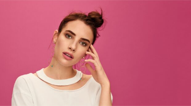 Emma Roberts posing with stylish earrings against a pink background