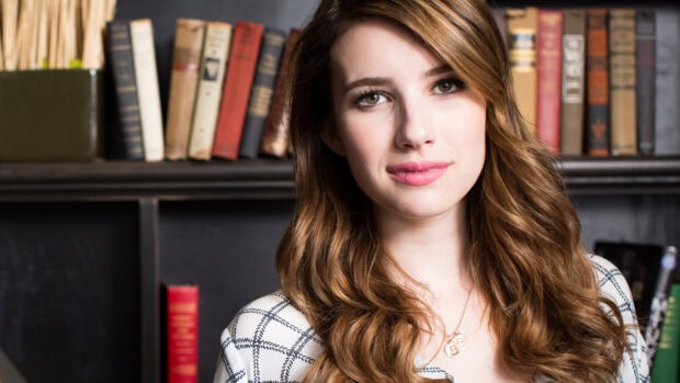 Emma Roberts posing with wavy hair in front of a bookshelf in a cozy setting