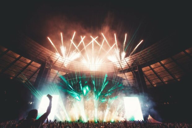 A lively festival crowd enjoying fireworks and laser lights inside a large stadium