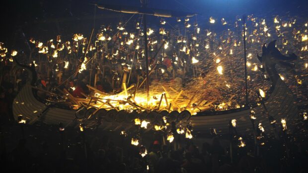Viking festival celebration with burning wooden ship and fire sparks at night
