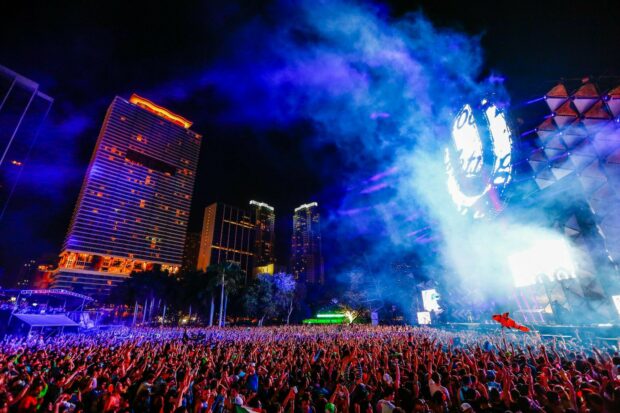 A large crowd enjoying festival at night with colorful lights and city buildings in the background
