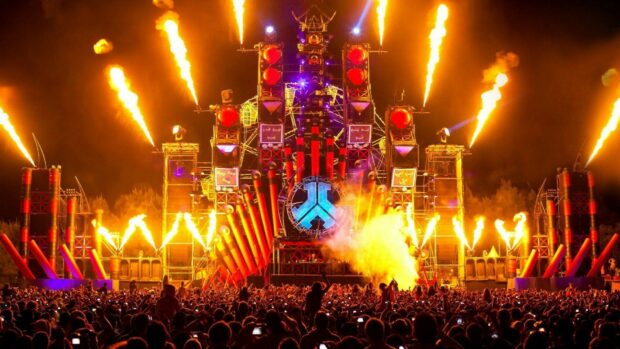 Large crowd enjoying a vibrant festival with fiery stage effects and colorful lights