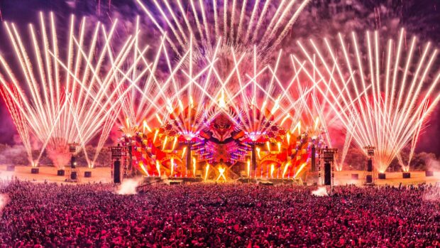 Large festival stage with fireworks lighting up the night sky over a massive crowd