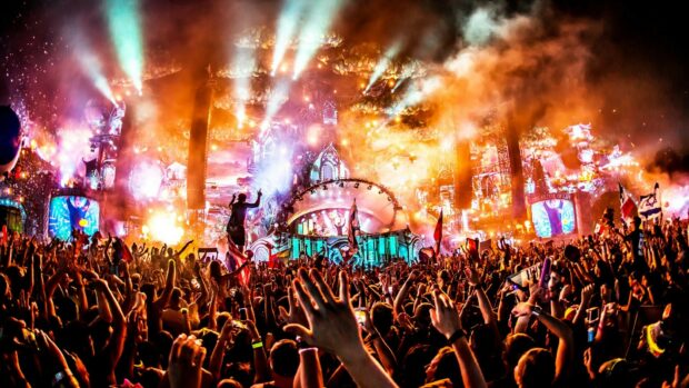 A large crowd enjoying music festival with colorful lights and smoke effects on stage