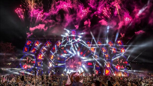A vibrant festival crowd enjoying a colorful light show with fireworks and stage displays