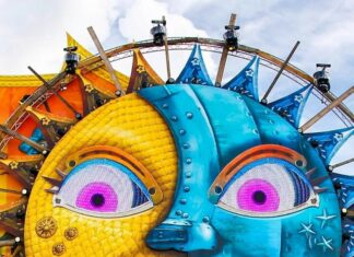 A lively festival crowd enjoys a colorful sun and moon art installation at an outdoor event