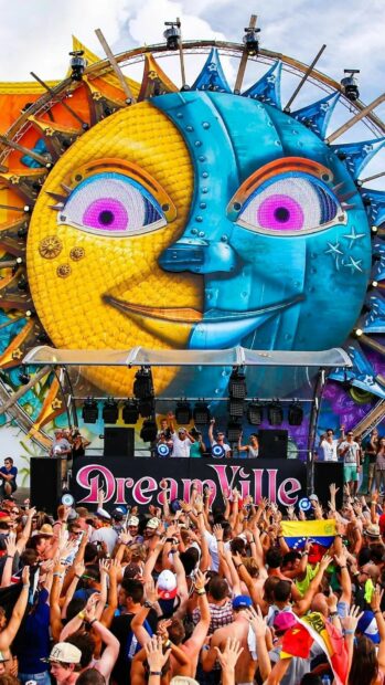 A lively festival crowd enjoys a colorful sun and moon art installation at an outdoor event