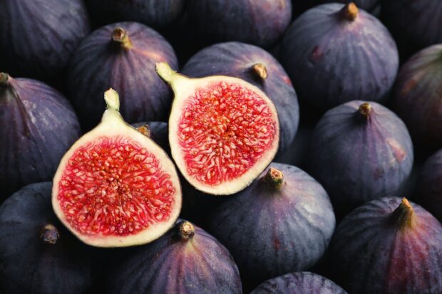 Fresh figs with a cut fig showing red seeds on a pile of whole figs